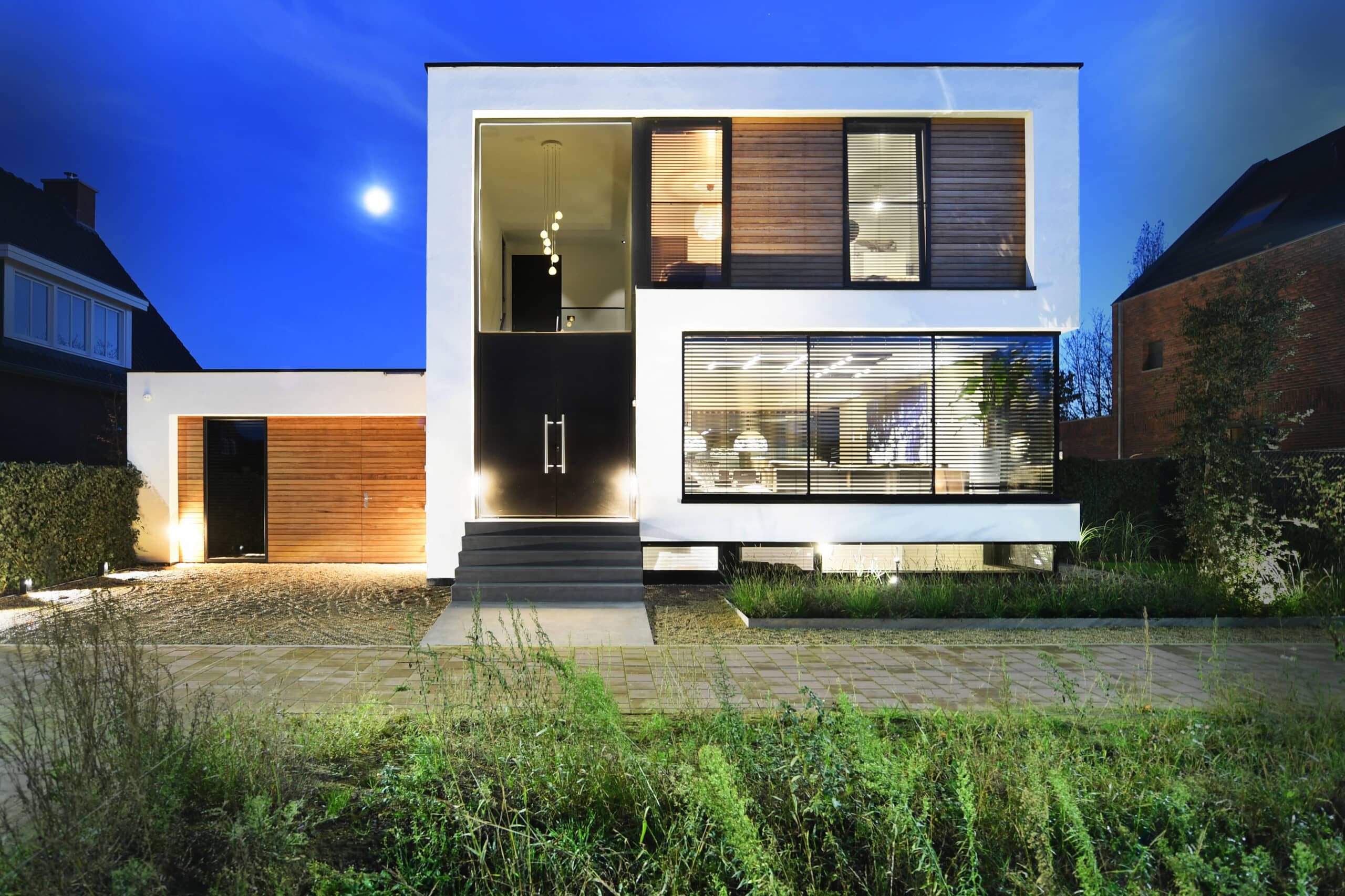 Moderne villa in Nederland met strakke lijnen, grote ramen en houten accenten, verlicht in de avond.