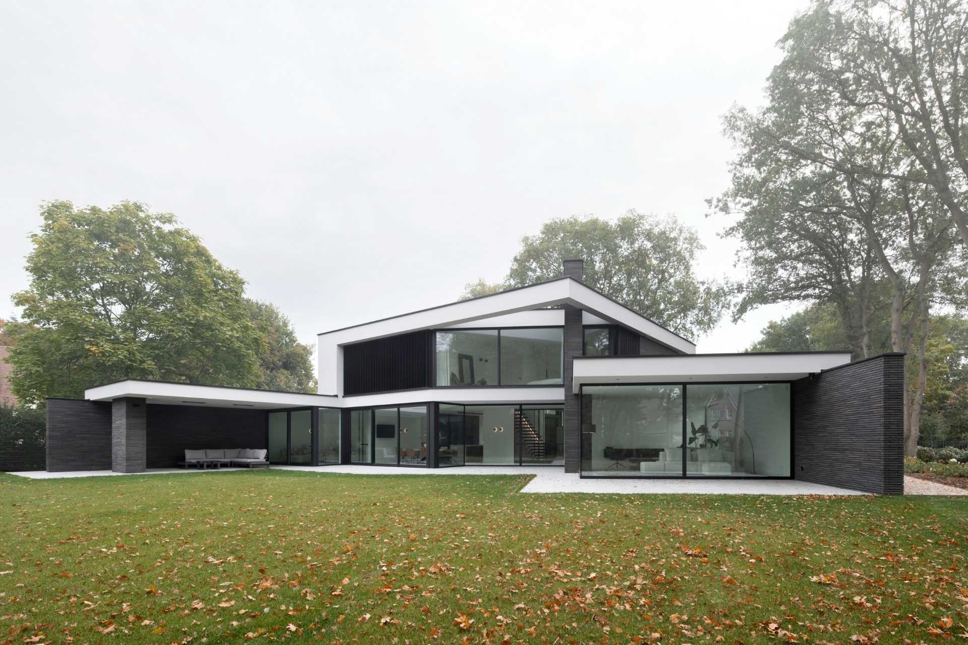 Achterkant van villa anglehouse achtertuin bossen transparant glas beton natuursteen gras