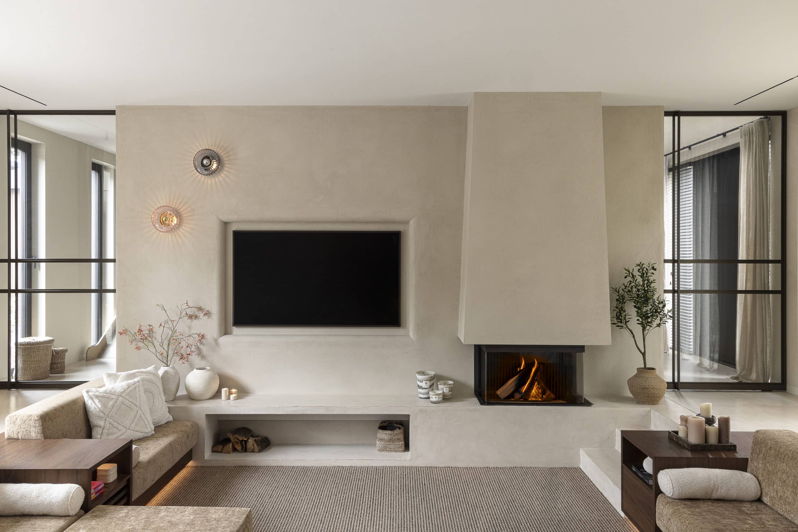 Luxe woonkamer van Bosvilla Waalre met haard, maatwerk tv-wand en warme neutrale tinten.