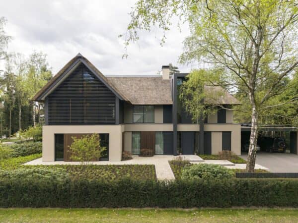Moderne villa in Zuid-Holland met rieten dak, donkere geveldetails, grote raampartijen en groene tuin rondom de woning.